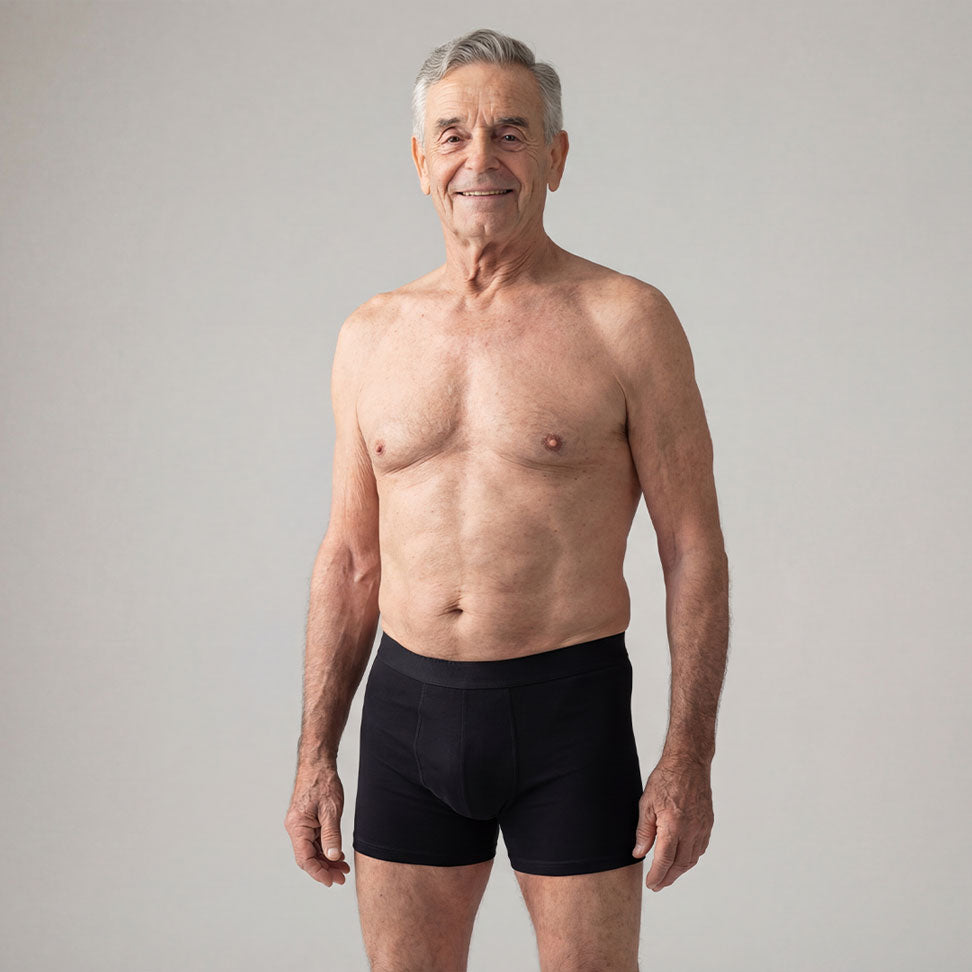 Homme senior souriant portant un boxer noir ultra absorbant Orykas sur fond neutre, illustration d’un sous-vêtement discret, lavable et confortable conçu pour les fuites urinaires légères à modérées.