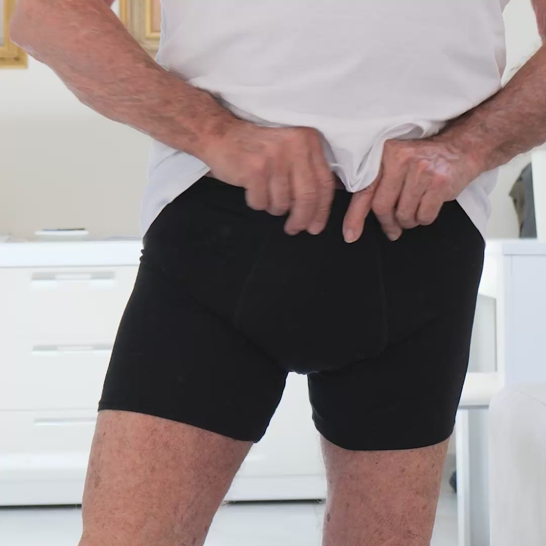 Homme adulte essayant un boxer absorbant Orykas dans une chambre, ajustant la ceinture pour vérifier le confort et le maintien, démonstration d’un sous-vêtement discret et lavable conçu pour les fuites urinaires légères à modérées.